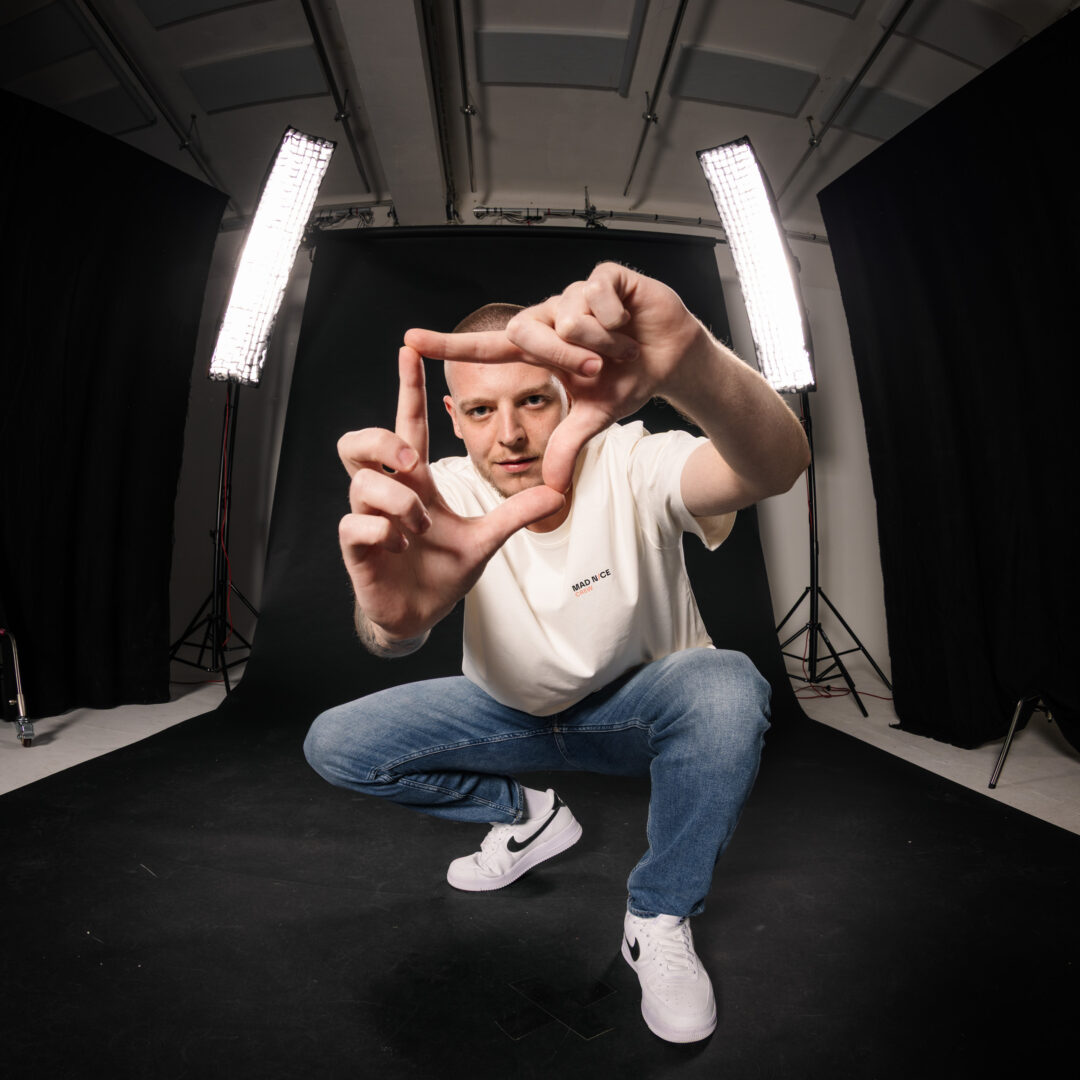 Teammitglied kniet lachend vor der Studiowand